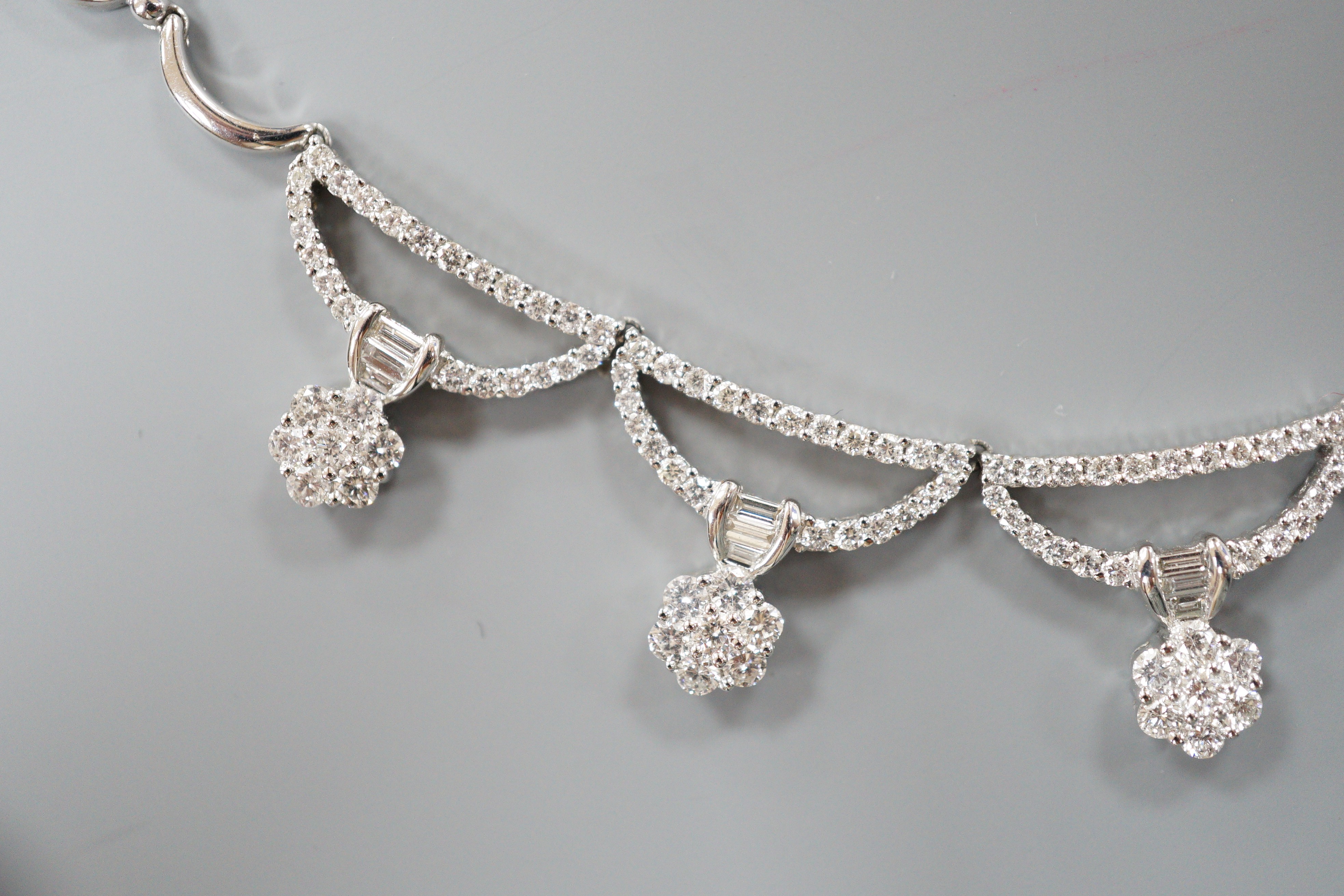 A modern 750 white metal and septuple baguette and round cut diamond cluster set curved link fringe necklace, 43cm, gross weight 26.6 grams